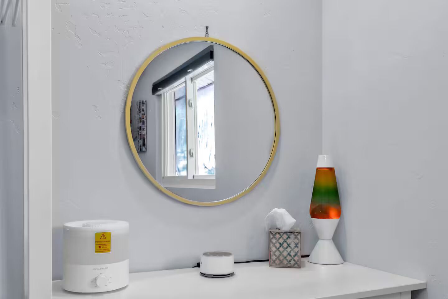 Een badkamer met een ronde spiegel, een witte wasbak, een lavalampe en een toiletrolhouder.