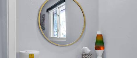 Een badkamer met een ronde spiegel, een witte wasbak, een lavalampe en een toiletrolhouder.