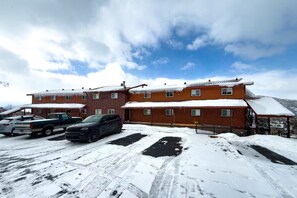 A multi-story building with a snow-covered roof and a parking area with several vehicles. - Alpine Edge, Top-Floor Ski Condo with Mountain Views adjacent to Ski Area (Steamboat Springs)