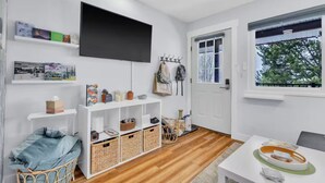 Quarto moderno e bem iluminado com televisão de tela plana, piso de madeira e janela com vista para árvores.