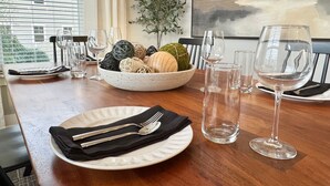 A dining table set with a white plate, black napkin, silverware, and wine glasses. A bowl with decorative balls and a plant is on the table. - Scenic Sky Retreat | EV Charger & Skyline Views (Chattanooga)