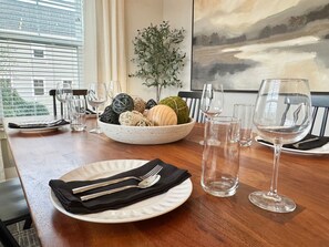 Une table à manger est dressée avec une assiette blanche, une serviette noire, des couverts et des verres à vin. Un bol contenant des boules décoratives et une plante sont posés sur la table.