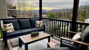 A balcony with a dark-colored sofa, a wooden coffee table, and a chair. - Scenic Sky Retreat | EV Charger & Skyline Views (Chattanooga)