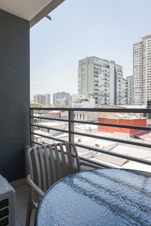 A balcony with a glass table and a chair, overlooking a cityscape with high-rise buildings. - 2BR/1BA Apartment Perfect for Families with Pool! (Ñuñoa)