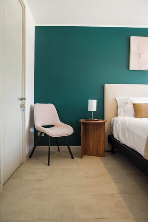 Ein Schlafzimmer mit einer türkisfarbenen Wand, einem Bett mit weißer Bettwäsche, einem Sessel und einem Nachttisch mit Lampe.
