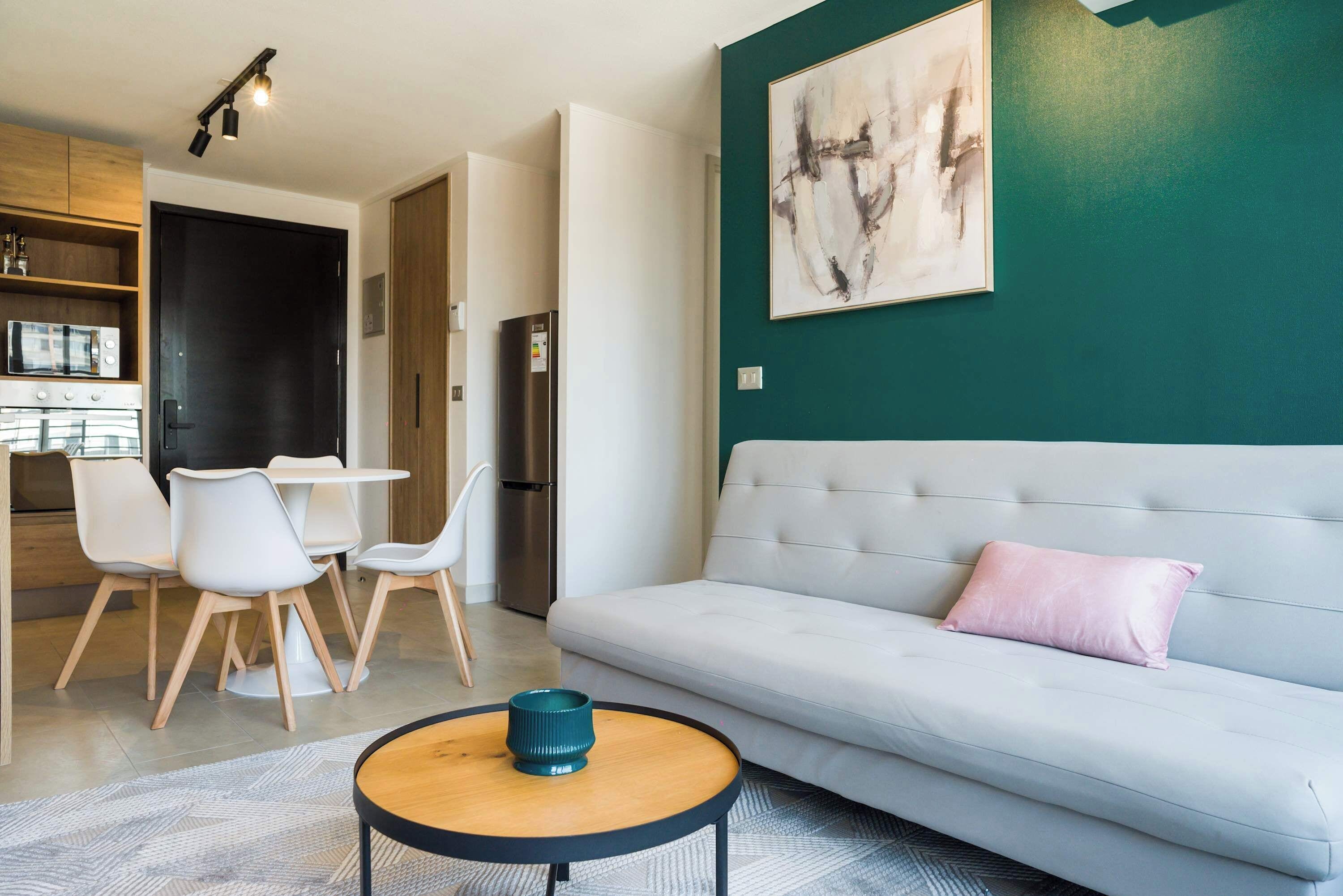 Una sala de estar moderna con un sofá blanco, una mesa de centro redonda y un comedor con sillas y una mesa blancos.