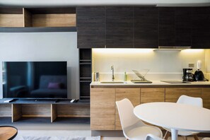 A modern kitchen with a built-in TV, wooden cabinets, a white countertop, and a dining area with white chairs. - 2BR/1BA Apartment Perfect for Families with Pool! (Ñuñoa)