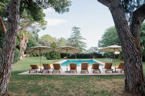 Área de piscina com espreguiçadeiras e guarda-sóis, cercada por árvores.