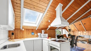 Cocina moderna con armarios blancos, estufa y microondas. Cuenta con un tragaluz amplio y vigas de madera en el techo.