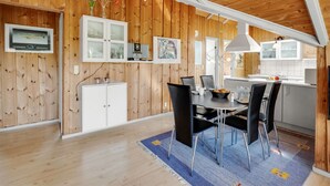 Una habitación con paneles de madera, una mesa de comedor, sillas y una zona de cocina.