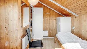 Un interior de madera con techo inclinado, una cama, un escritorio y una silla.