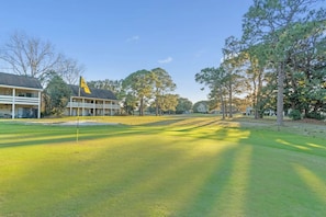 Un campo de golf con una bandera, árboles y un edificio con asta de bandera.