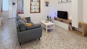 A modern living room with a grey sofa, a coffee table, and a TV. There is a ceiling light fixture and a wall-mounted air conditioner. - Amazing 2-bedroom apartment in adorable Monopoli with AC (Monopoli)