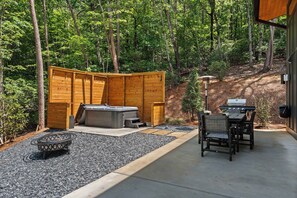 Eine Terrasse mit Whirlpool, Sitzgelegenheit im Freien und Grillbereich, umgeben von einem Holzzaun und Bäumen.
