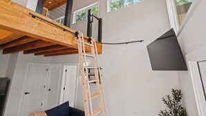 Ein Loft-Zimmer mit freiliegenden Holzbalken, einer Holzleiter und einem schwarzen Kabel an der Decke.