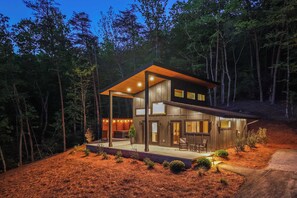 A modern two-story house with a covered porch, large windows, and a well-lit interior.