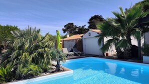 A swimming pool with clear blue water, surrounded by palm trees and a white building with a tiled roof. - Self-contained studio near the ocean with private heated pool (Saint-Denis-d'Oléron)