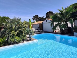 Ein Swimmingpool mit klarem, blauem Wasser, umgeben von Palmen und einem weißen Gebäude mit einem Flachdach.
