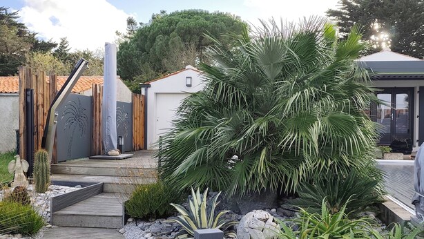 A garden pathway leading to a building with a modern design, surrounded by various plants and a wooden fence. - Self-contained studio near the ocean with private heated pool (Saint-Denis-d'Oléron)