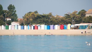 A row of colorful beach huts along a sandy beach with a clear blue sky. - Self-contained studio near the ocean with private heated pool (Saint-Denis-d'Oléron)