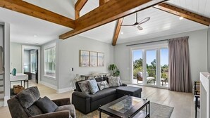 A spacious living room with a sectional sofa, a glass coffee table, and a ceiling fan. - Stunning Vacation Home Just Steps to the Beach! (Hilton Head Island)