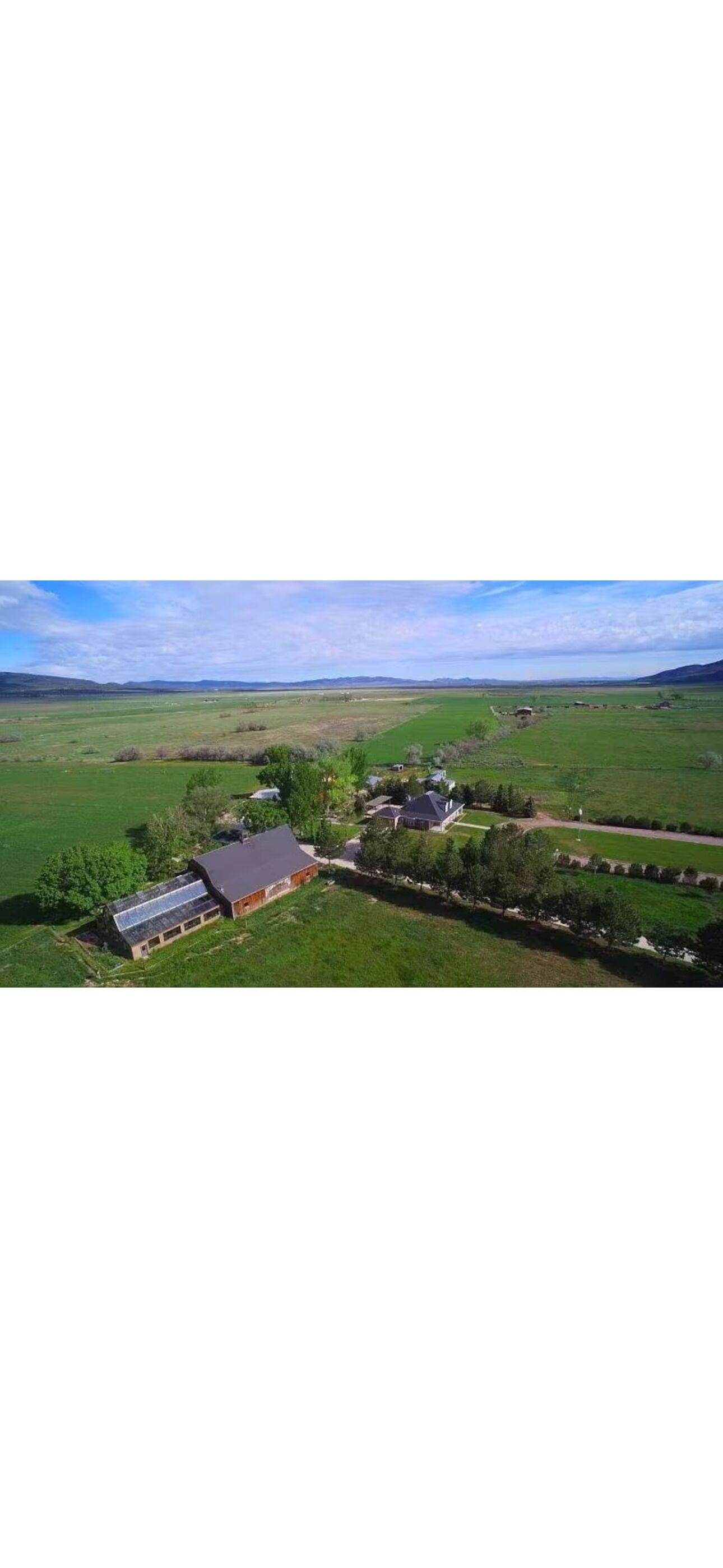 Vista aérea de una propiedad rural con un gran granero, campos abiertos y algunos árboles dispersos.