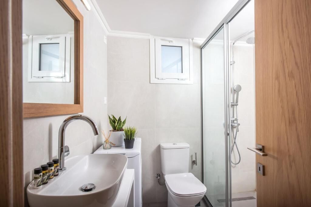 Uma casa de banho moderna com lavatório, espelho, sanita e chuveiro.