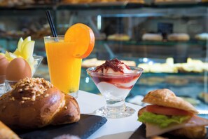 A breakfast setting with a croissant, a sandwich, a glass of orange juice, and a dessert in a glass. - Loggia Suites (Heraklion)