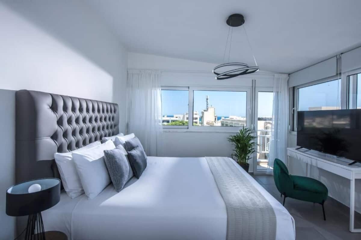 Ein modernes Hotelzimmer mit einem großen Bett, einem Fernseher, einem Schreibtisch und Blick auf die Stadtlandschaft.