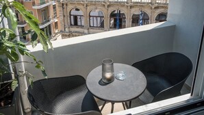 A balcony with two black chairs and a small table, overlooking a historic building with arches. - Loggia Suites (Heraklion)
