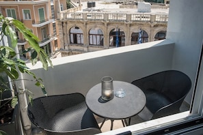 A balcony with two black chairs and a small table, overlooking a historic building with arches.