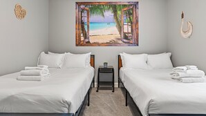 A hotel room with two beds, white linens, a small table with a plant, and a painting of a beach scene. - Lucayan Harbour Kissimmee Home with Pool, Sleeps 12, Near Disney World (Kissimmee)