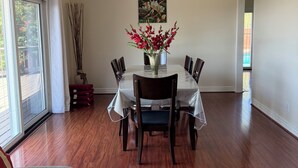 Un comedor con una mesa, sillas, un florero con flores, un cuadro en la pared y vistas al exterior por una ventana.