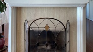 Una chimenea con una celosía metálica decorativa, un reloj y un jarrón sobre la repisa.