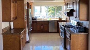 Una cocina amplia con armarios de madera, un refrigerador de acero inoxidable, lavavajillas, estufa a gas y una araña.