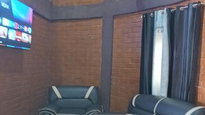 A room with brick walls, a flat-screen TV mounted on the wall, and a seating area with black leather sofas.