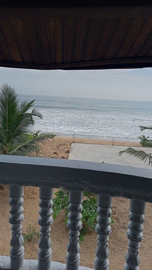 Vista a la playa desde un balcón con techo de madera, palmeras y una playa de arena.