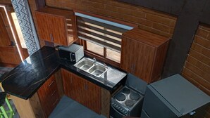 A compact kitchen with wooden cabinets, a black countertop, a microwave, a sink, and a stove.