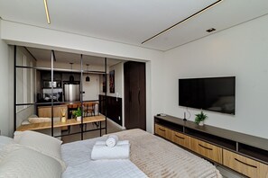 A modern bedroom with a bed, a TV, a desk, and a kitchenette. - Loft Moderno Centro Itajaí (Itajaí)