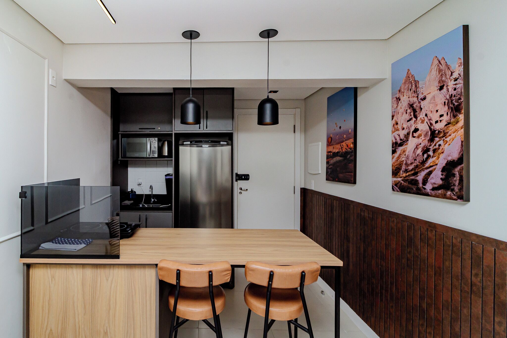 A modern kitchen with a wooden island, two pendant lights, and a refrigerator.