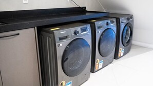 A row of front-loading washing machines in a laundry room with a black countertop above them. - Loft Moderno Centro Itajaí (Itajaí)