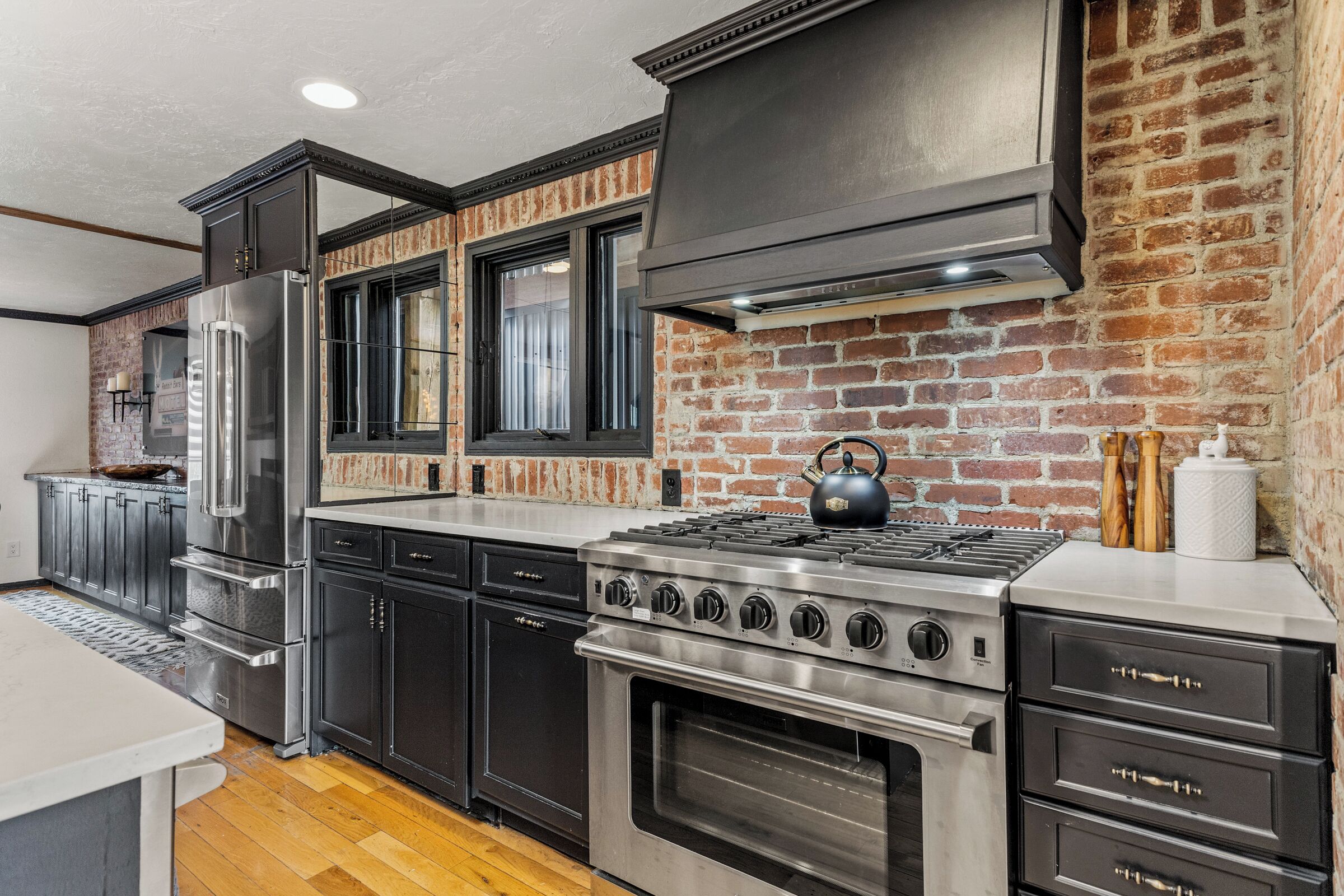 A modern kitchen with stainless steel appliances, dark cabinetry, and a brick accent wall.