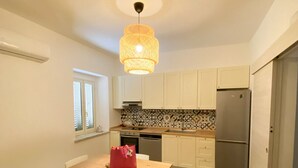 Une cuisine compacte avec des meubles blancs, un îlot central doté de chaises, un luminaire suspendu et un réfrigérateur.