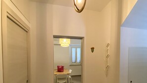 Un couloir avec une porte en bois sur la gauche, une porte blanche sur la droite, et une table avec des chaises au fond.