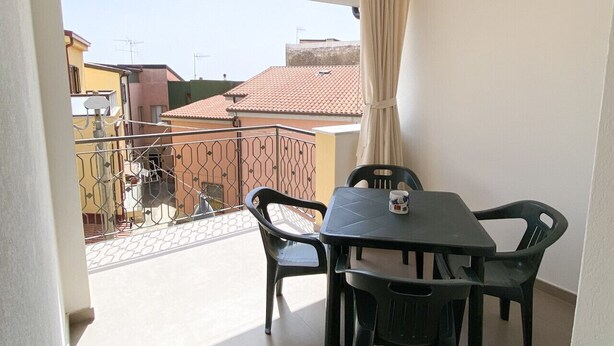 Un balcon avec une table et des chaises, une vue sur les bâtiments voisins et un ciel dégagé.