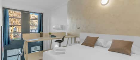 A modern hotel room with a bed, a desk, and a view of the outside.