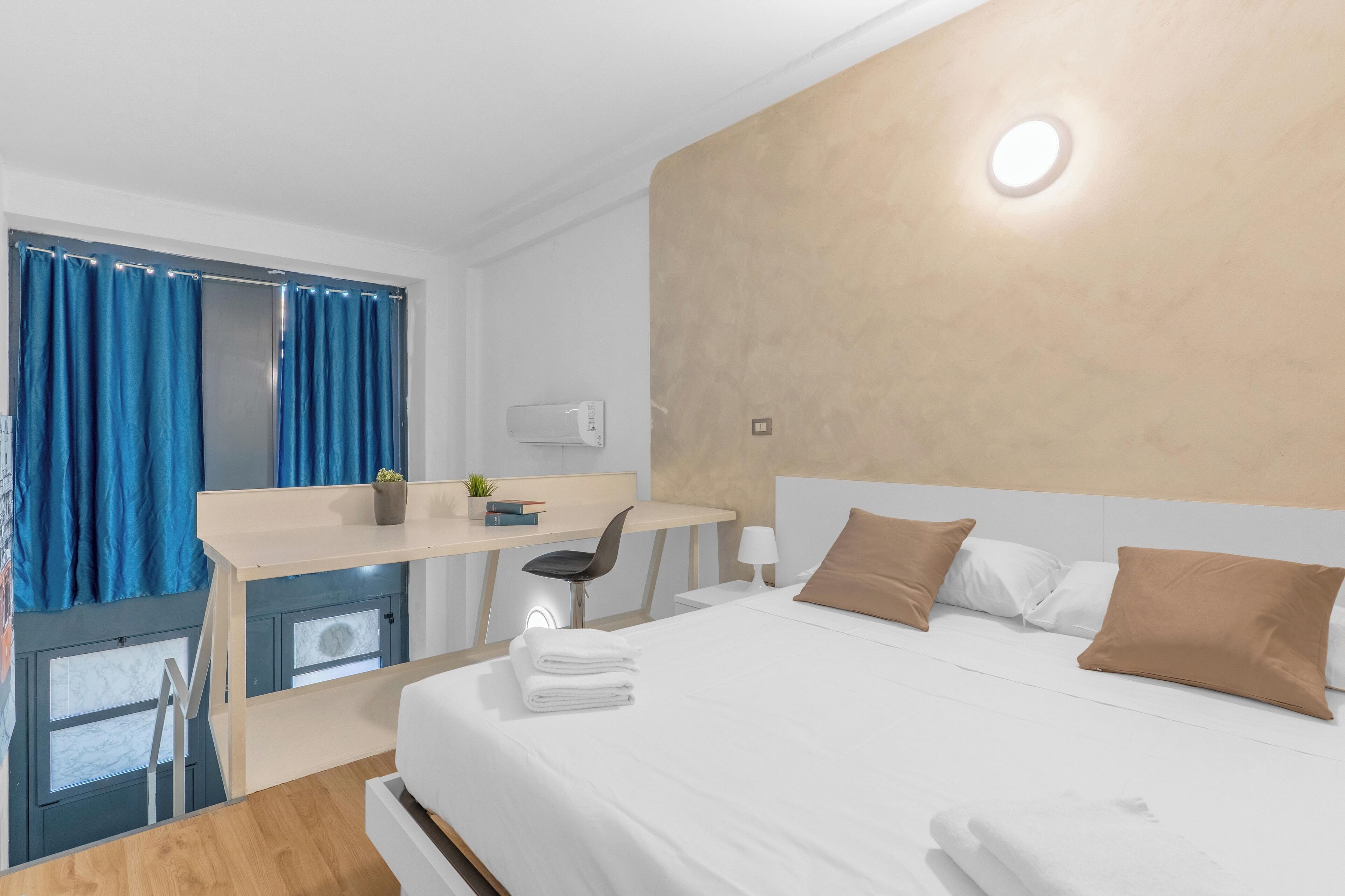 Quarto de hotel com cama, escrivaninha, cadeira e pequena mesa com uma planta.