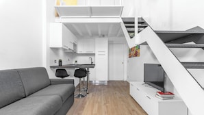 Un appartement moderne avec un canapé gris, un coin repas comprenant une table et des chaises, une cuisine et un escalier menant à un niveau supérieur.