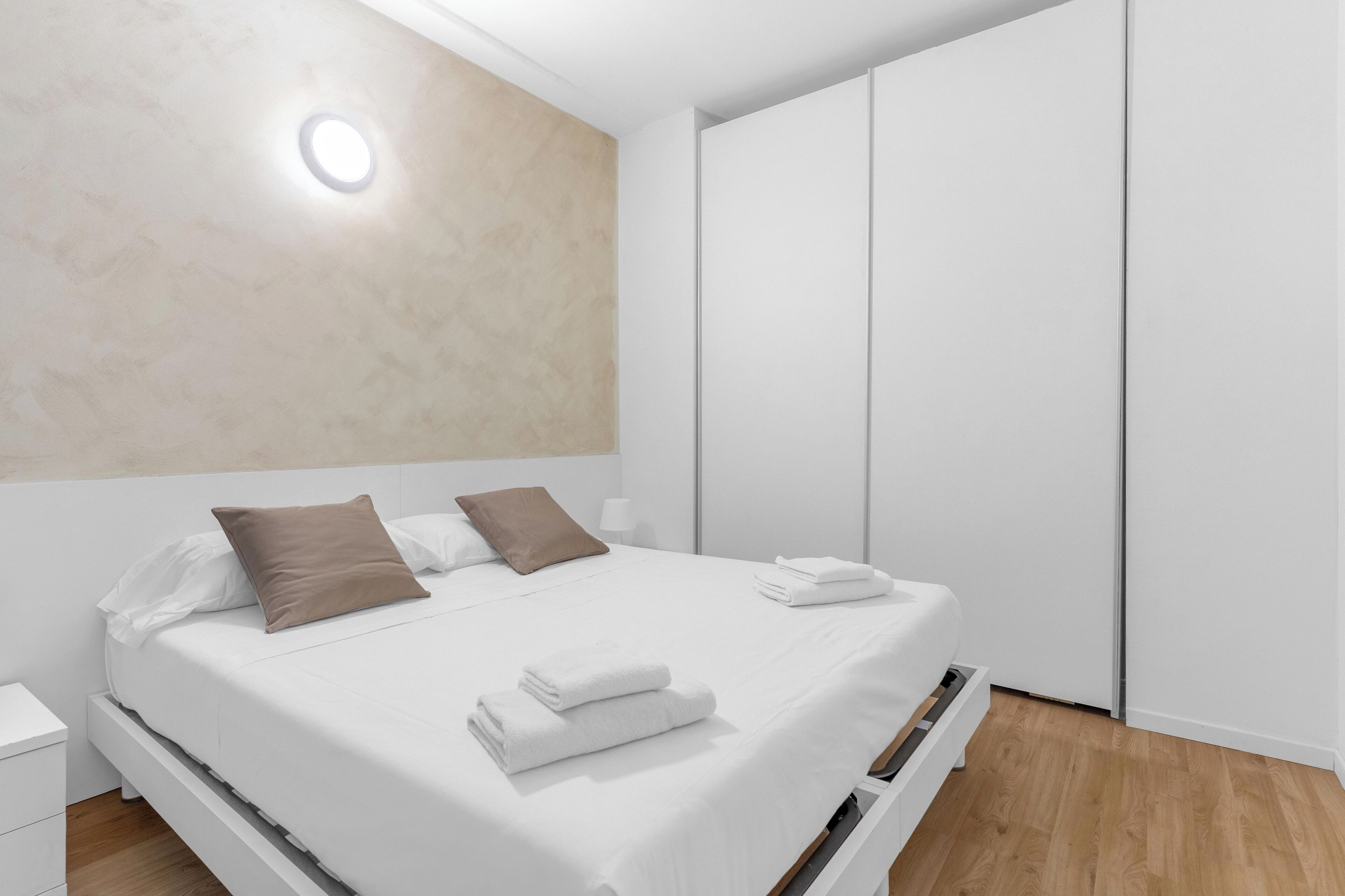 Un dormitorio moderno con cama, mesitas de noche blancas, suelo de madera y un armario.