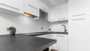 Une cuisine moderne avec des meubles blancs, un plan de travail noir, un four à micro-ondes et un évier.